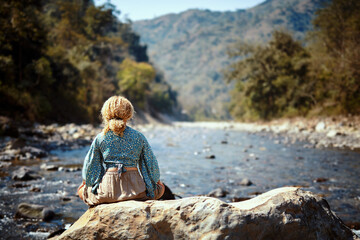 Woman meditating on a rock near a river, embraced by the beauty of nature and the peaceful atmosphere of the mountains.