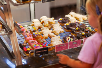 little girl looking at iced and decorated doughnuts in shop window