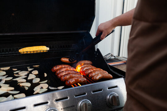 man cooking fat sausages from local butcher on bbq in backyard with corn and chips