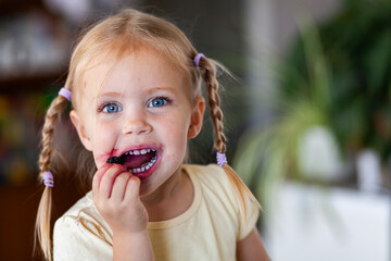 Toddler kid eating fresh picked mulberries inside home with purple juice on face and teeth