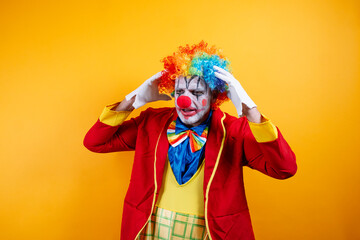 A pensive, sad adult clown on a vibrant yellow background.