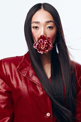 Seductive woman with long black hair in a red leather jacket and a flower in her mouth posing...