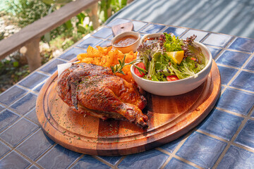 Half chicken baked in oven with mixed garden salad and french fries on wooden tray