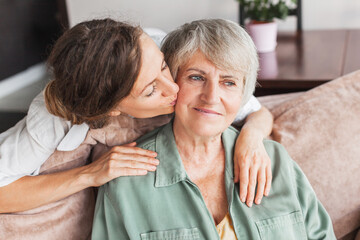 Adult girl child kiss overjoyed middle-aged mom relaxing together on sofa in living room