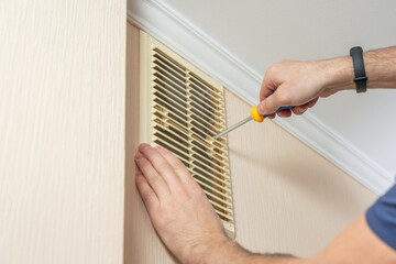 A man installs a plastic ventilation grid into a hole in a wall