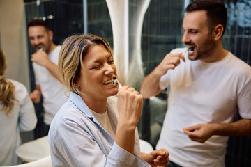 Happy woman laughing while brushing teeth with her husband in morning.