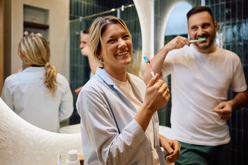 Cheerful woman brushing teeth with her husband in  bathroom.