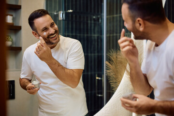 Reflection in  mirror of happy man applying face cream in  morning.