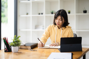 education, online, studying, E learning, young Asian woman having video call on her computer at home. Girl reading book preparing exam test having online consultation, education and learning concept.
