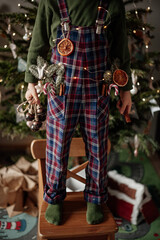 A boy staying on a chair in the Christmas decorations holds bells in his hand