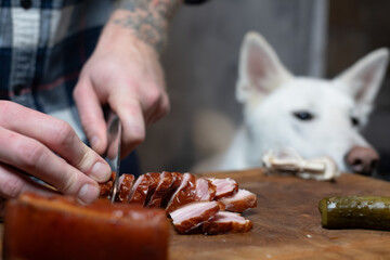 Man slicing smoked bacon, dog watching