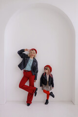 A woman and a girl are standing against the wall, the girls are looking at their mother and wearing glasses