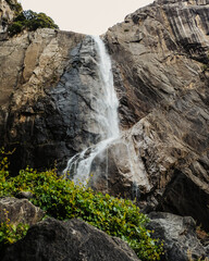 Waterfall cascading down a rugged cliff surrounded by pine trees. Mountain landscape under a clear sky