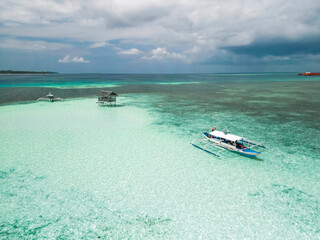 An aerial view of a traditional Filipino outrigger boat (bangka) anchored in shallow, crystal-clear turquoise waters under a bright sky in Balabac, Philippines