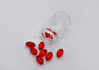 Red capsules scattered from a jar on a white background