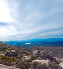 Mountain landscape from the summit of La Maliciosa with impressive rock formations, wild vegetation, and a partly cloudy sky. A panoramic view of mountains and a lake, ideal for hiking and nature love