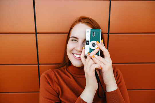 Smiling woman photographing with camera in front of brown wall
