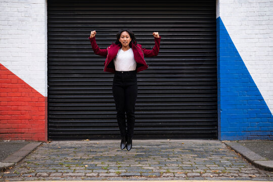 Happy woman flexing muscles and jumping in front of shutter