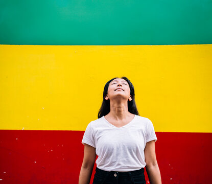 Smiling woman standing with eyes closed in front of multi colored wall