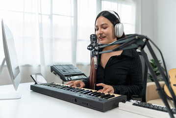 Professional Women Musician composing a song with acoustic guitar, piano keyboard and condenser microphone. She mixing and mastering her song with table at digital recording home studio.