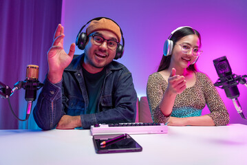 Two young asian streamer host making live podcast with condenser microphone and tablet at broadcast...