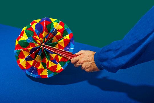 Hand of man holding colorful fan over blue table against green background