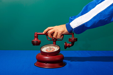Hand of man using maroon colored retro style telephone alarm clock kept on blue table
