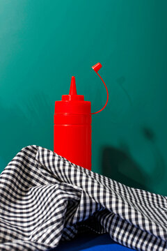 Tomato ketchup bottle with gingham tablecloth in front of green background