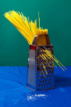 Spaghetti in food grater in front of green background