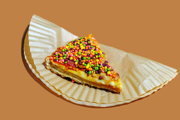 Still life of a sweet candy pizza slice with colorful sprinkles on a paper background