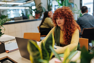 Focused young businesswoman working on laptop in modern green office