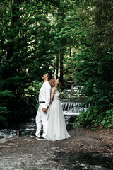 A large waterfall with very cold water and slippery stones, its height is more than 8 meters, the bride and groom are standing on the stones, this photo was taken with a long exposure