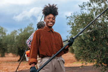 Young farmer harvesting olives with coworker in background
