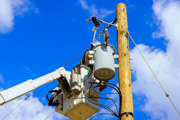 Municipal power worker in hydraulic lift conducts an inspection of high voltage equipment.