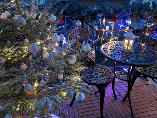  cozy balcony decorated for new year, featuring glowing tree adorned with ornaments and twinkling lights. Festive garlands, lanterns, and sparkling decorations create warm holiday atmosphere under nig