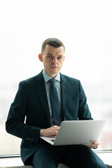 Successful smiling ambitious caucasian european businessman lawyer in suit standing in light office with laptop and phone