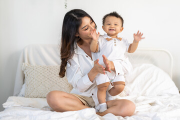 Portrait of enjoy happy love family asian mother playing with adorable little asian baby.Mom touching with cute son moments good time in a white bedroom.Love of family concept