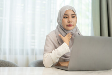 Muslim woman in hijab working on laptop sitting at desk in cozy home office, study on her task, freelance work, online education, remote work from home, modern muslim female business professional