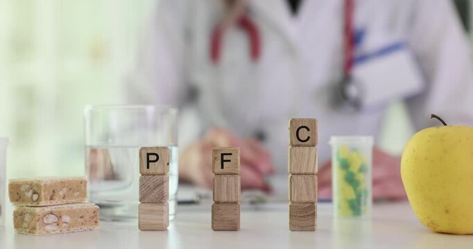 Letters PFC for proteins fats carbohydrates on wood blocks on nutritionist desk. Woman doctor marks notes at table with food supplements