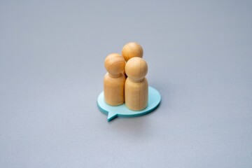 Three wooden figures standing on a blue speech bubble, symbolizing a group consensus or shared...