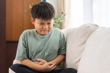 Portrait of sick unhappy little child asian boy touching belly stomach with suffering from stomach...