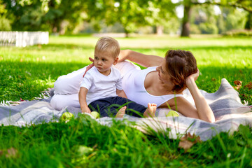 Mom in white clothes rests with her child in the park on green grass. Happy parenting outside. Lifestyle.