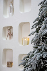 Modern Christmas interior with a focus on details: snow-covered branches of a Christmas tree with shimmering garlands and pearl decor. In the background, a wall with decorative niches decorated with a