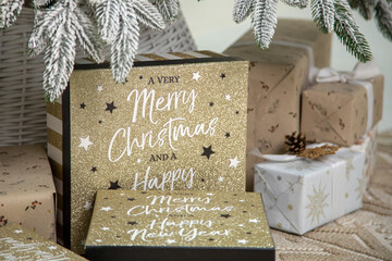 Festive Christmas gift arrangement featuring gold glittery boxes with the text 'Merry Christmas and a Happy New Year,' surrounded by beautifully wrapped presents in neutral tones, set under a frosted 