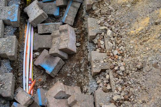 Construction site showing a trench filled with gravel and concrete blocks, revealing optical fiber pipes underneath.