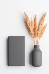 A minimalistic arrangement featuring a gray notebook beside a decorative vase with dried grass, set against a light background.