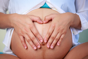 Pregnant woman forming heart shape on her belly, expressing love and joy