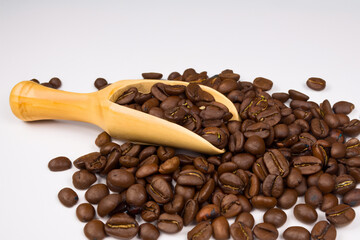 Obraz premium Coffee beans with a wooden spoon. A white spoon with coffee beans on a white background. Coffee beans spoon white background brown lies wood. A spoon lying on a wooden background with brown lifestyle.