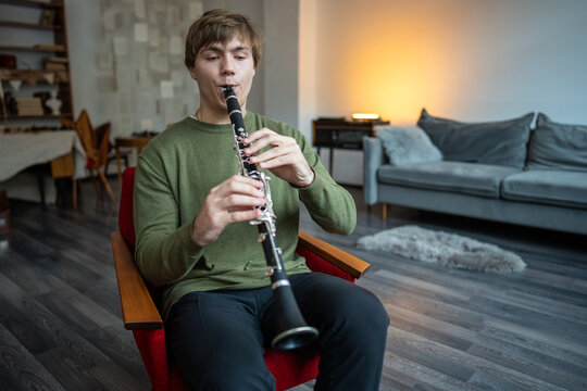 Clarinet player. Concentrated clarinetist playing flute woodwind music instrument sitting on armchair at home. Musical instruments. Man plays the oboe in living room. Relaxed mental hobby concept