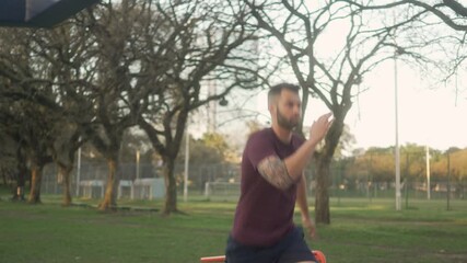 man in a maroon shirt performing jumping switch exercises in an outdoor park. Athletic individual finishing a workout session and taking a moment to rest in nature.